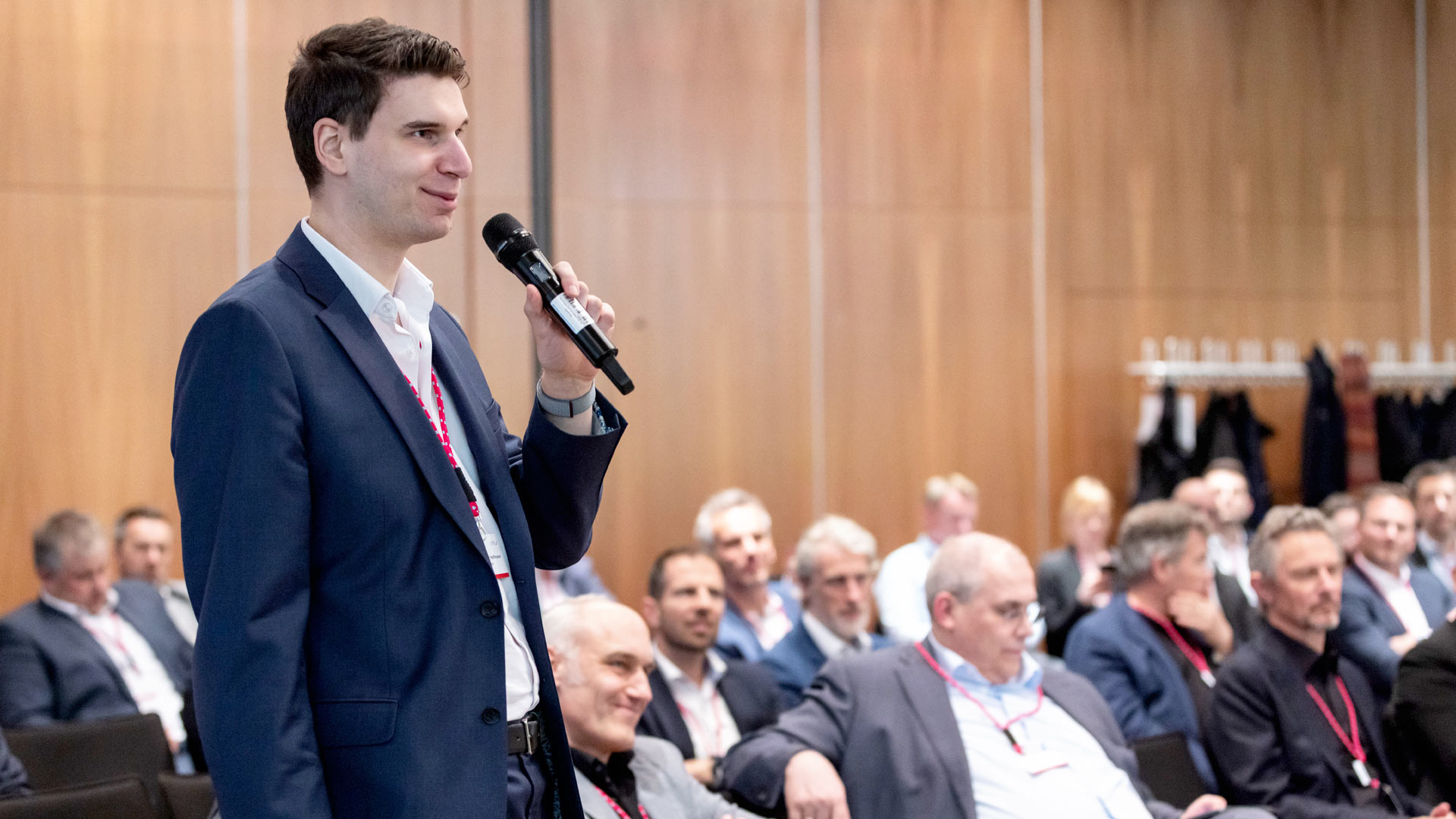 Frage aus dem Publikum. Mann mit Mikrofon stehend, umrandet von Plenum.  