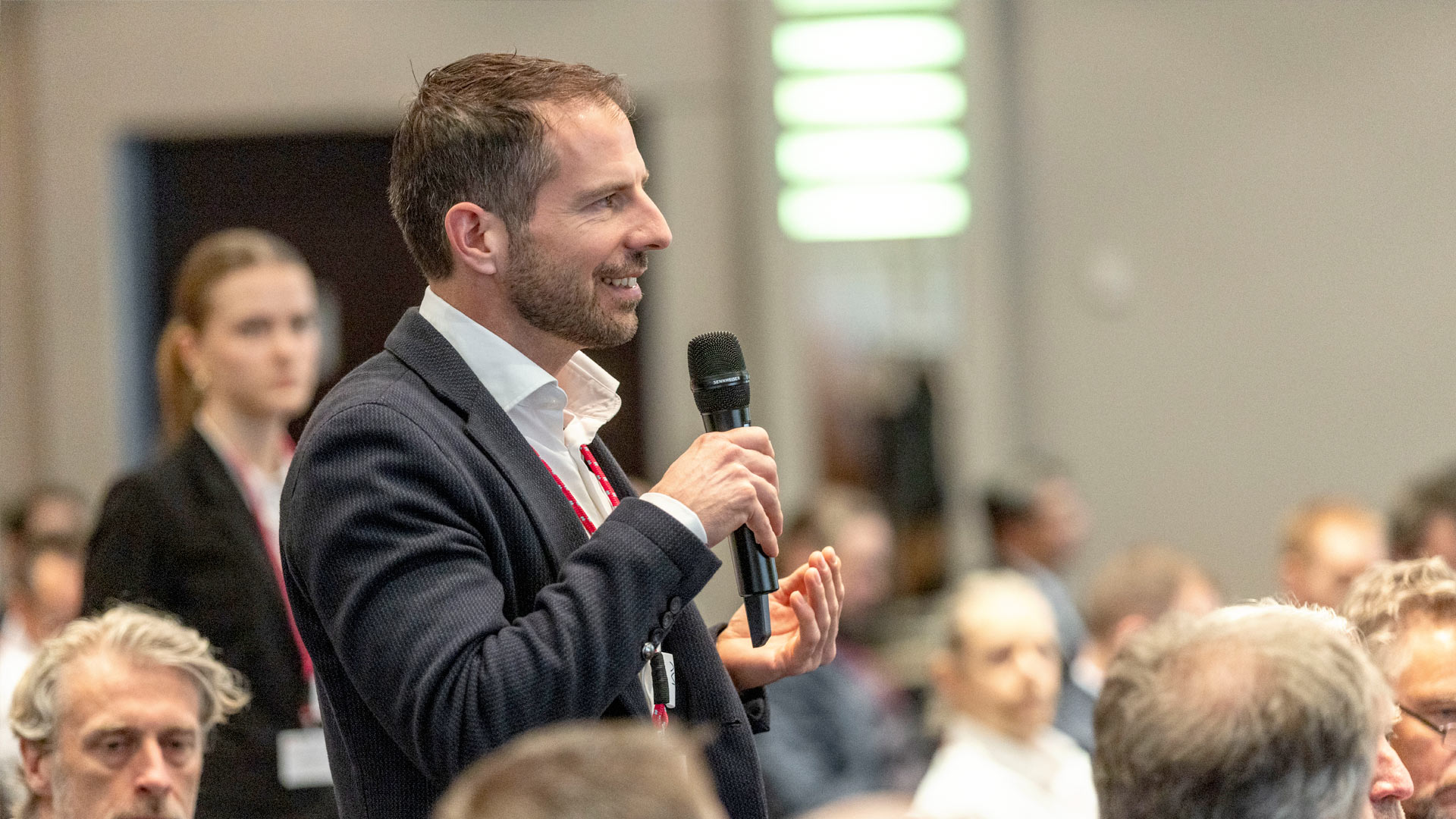 Question from the audience. Man with microphone standing, surrounded by plenum.