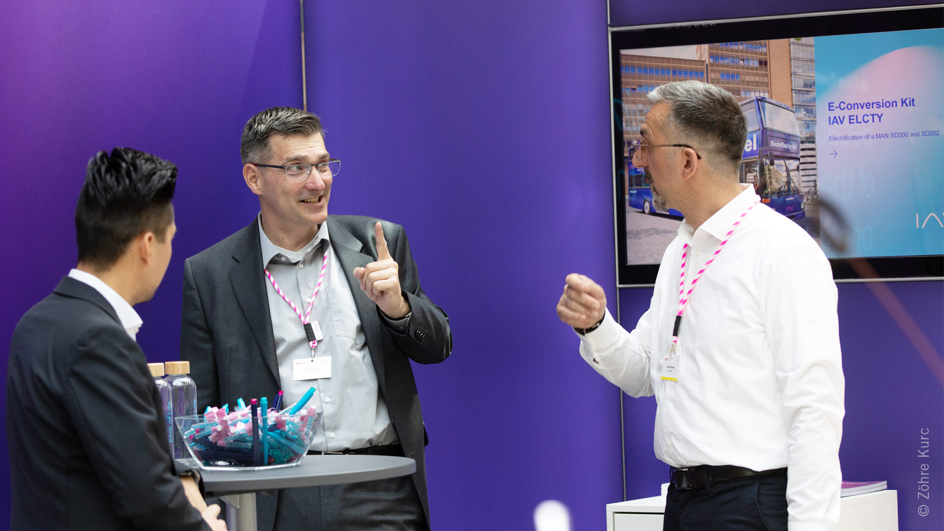Three gentlemen in conversation at an exhibition stand.