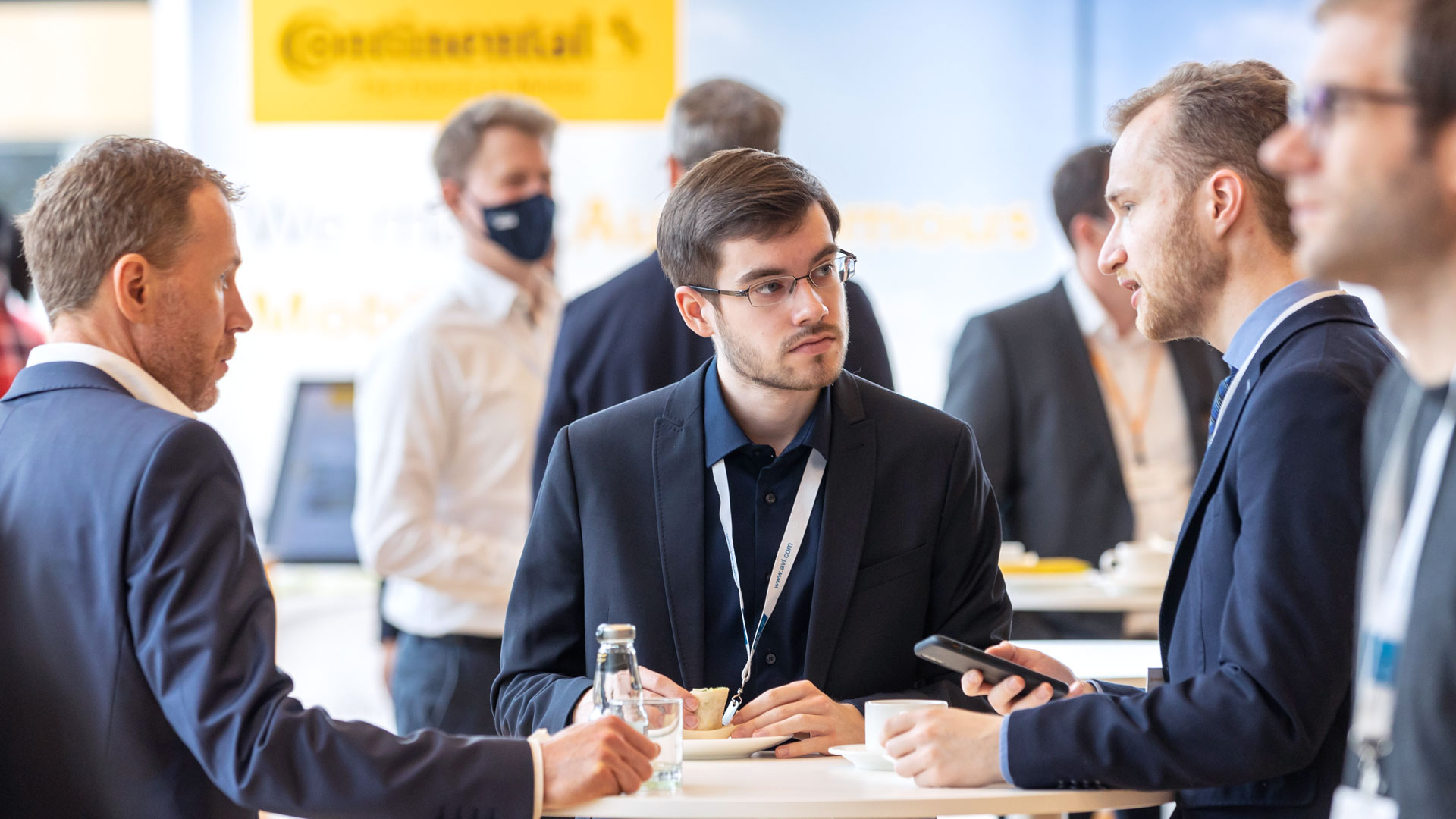 Mehrere Gruppen von Menschen im Ausstellungsbereich umgeben von Ständen und Exponaten.