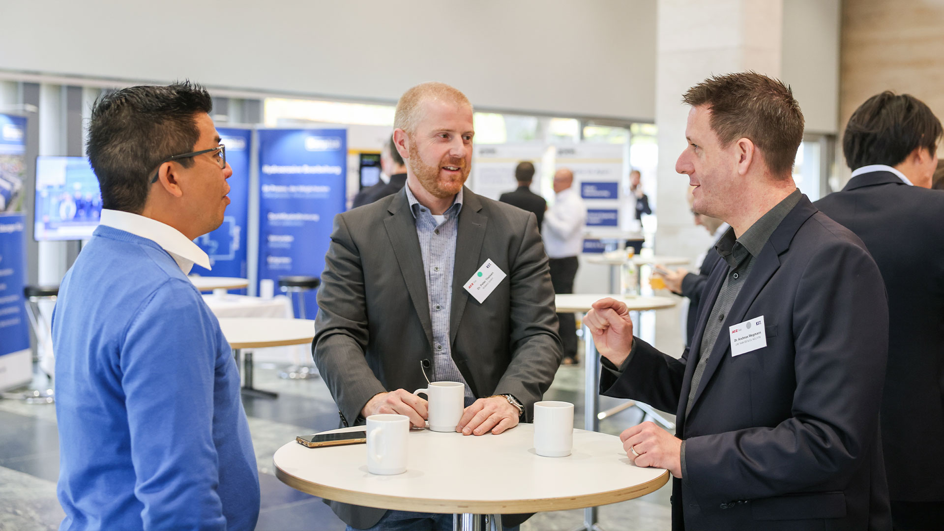Three conference participants in conversation at a bistro table during the coffee break. 