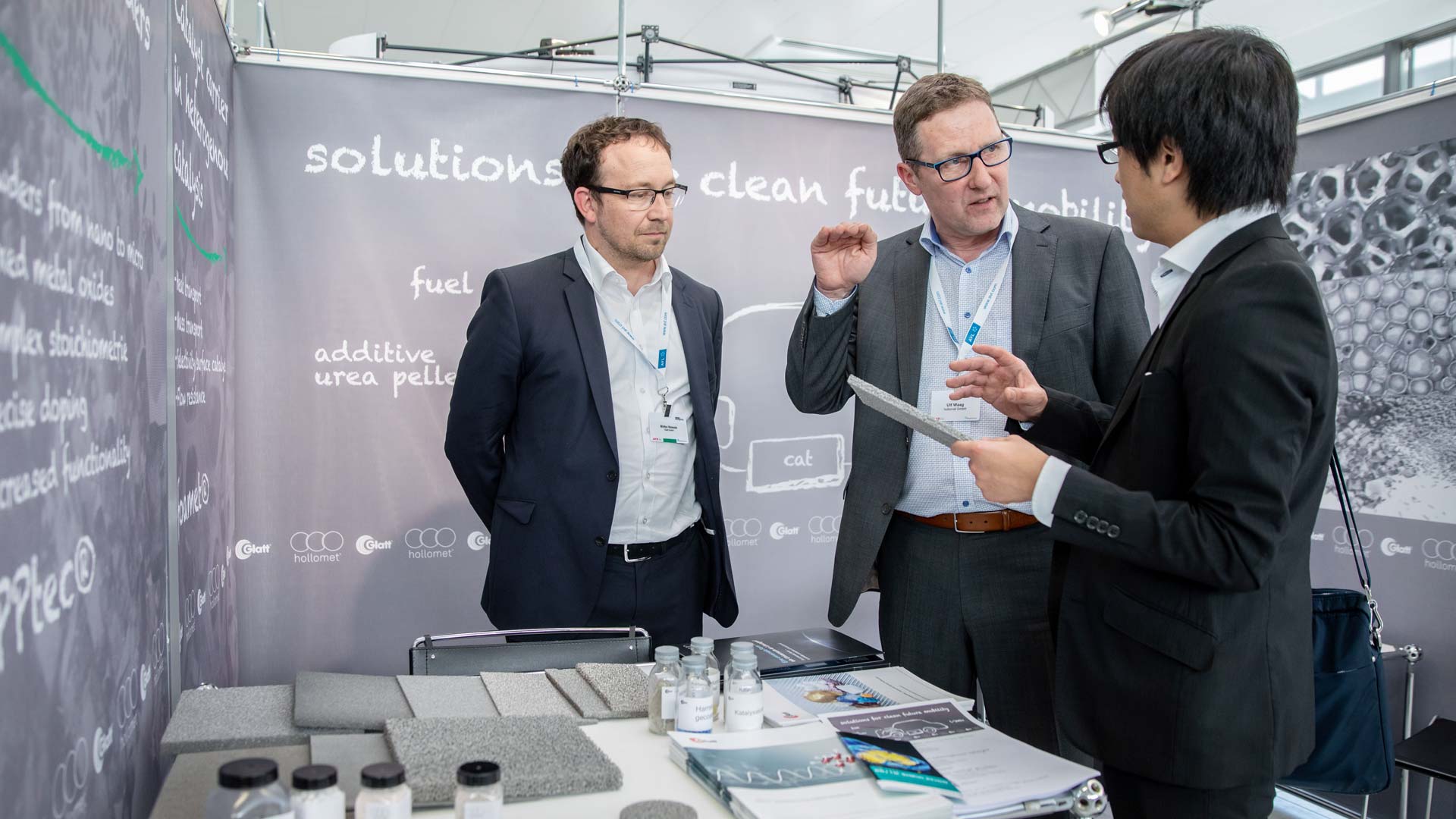 Three gentlemen in conversation at an exhibition stand.