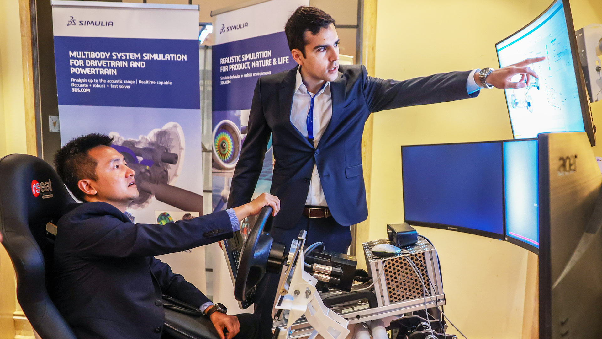 Mann sitzend in einem Fahrsimulator im Ausstellungsbereich bekommt Produkt erklärt. 