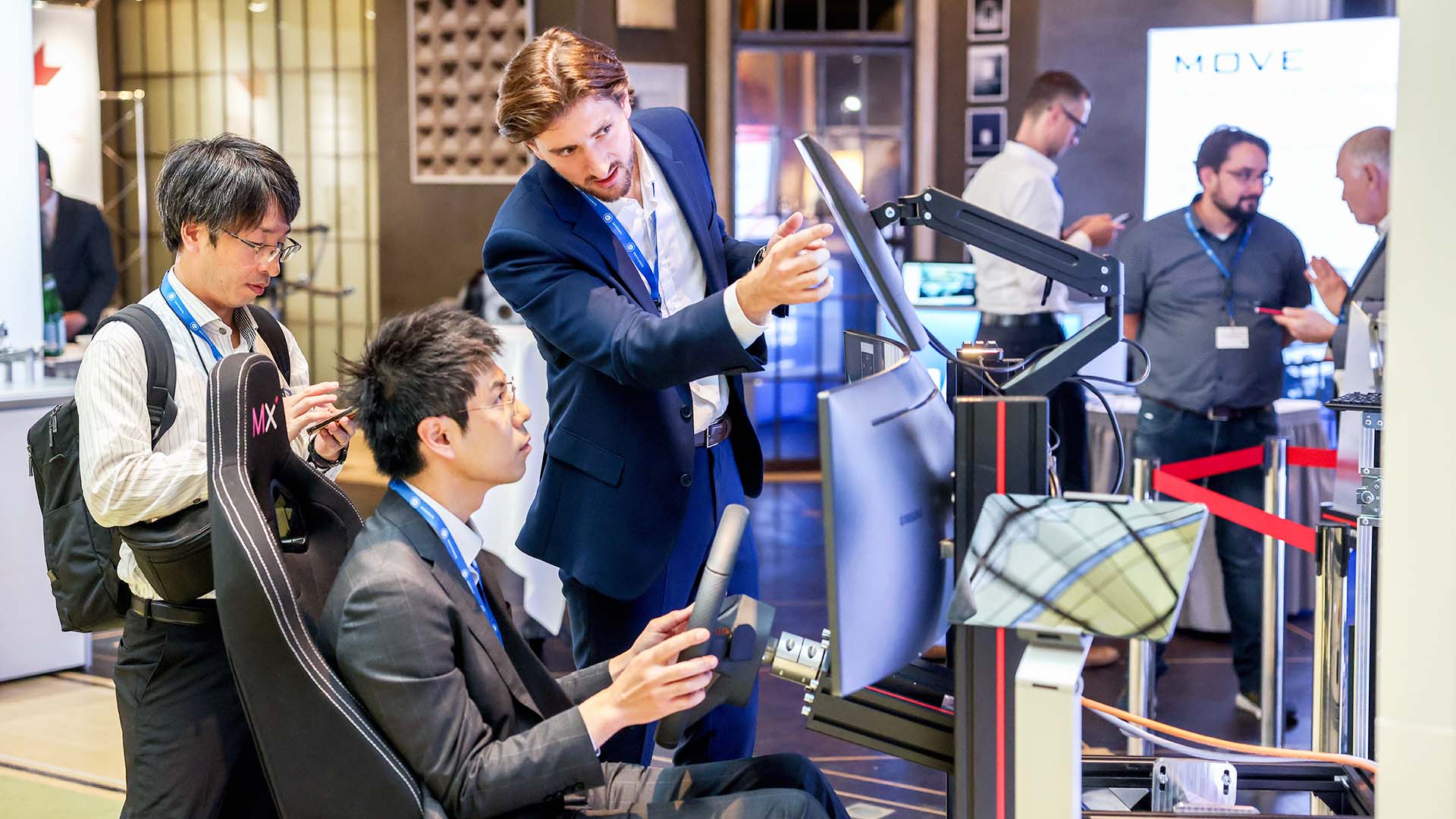 Mann sitzend in einem Fahrsimulator im Ausstellungsbereich bekommt Produkt erklärt. 