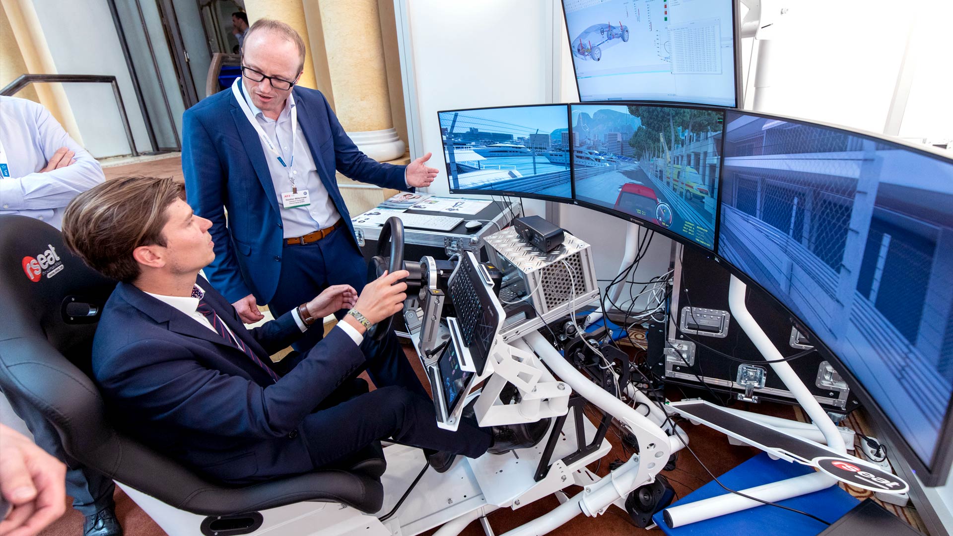 Mann sitzend in einem Fahrsimulator im Ausstellungsbereich bekommt Produkt erklärt. 